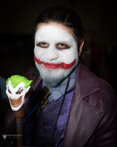 a man with clown makeup on his face and holding a toy in his hand while wearing a purple jacket