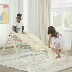 two children playing on a wooden slide in a room with striped wallpaper and white curtains