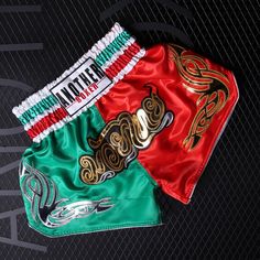 two muay thai boxing shorts with gold and red designs on the front, one in green and one in red