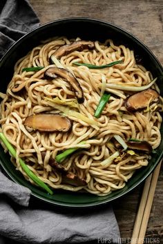 a bowl filled with noodles and mushrooms on top of a table next to chopsticks