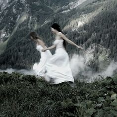 two women in white dresses are walking through the mountains