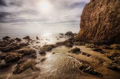 the sun shines brightly through the clouds over some rocks and water at the beach