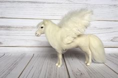 a small white horse with wings on it's back standing on a wooden floor