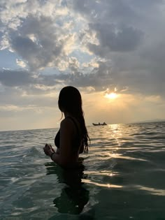 a woman is sitting in the water at sunset