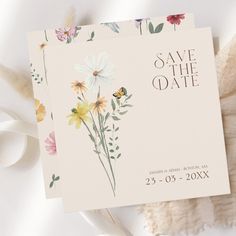 save the date cards with watercolor flowers on them next to some feathers and petals