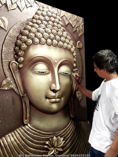 a man is painting the face of a buddha statue with gold paint on it's side