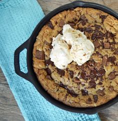 a chocolate chip cookie in a cast iron skillet with ice cream on top and a blue towel next to it