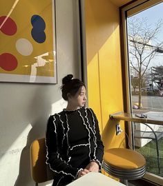 a woman sitting at a table in front of a window with a painting on the wall