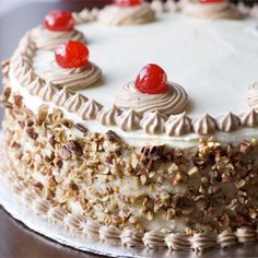 a cake with white frosting and cherries on top is sitting on a table