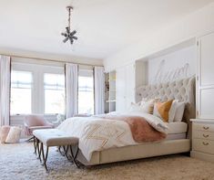 a bedroom with a bed, dressers and two chairs next to each other in front of large windows