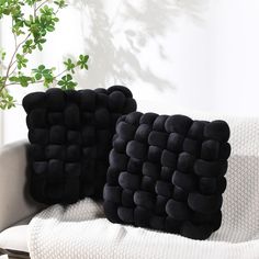 two black pillows sitting on top of a white couch next to a potted plant