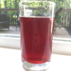 a glass filled with red liquid sitting on top of a table next to a window