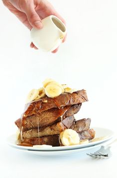 a stack of french toast with bananas and syrup being drizzled on top