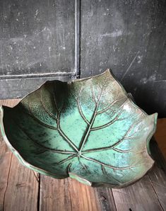 a green leaf shaped bowl sitting on top of a wooden table next to a wall