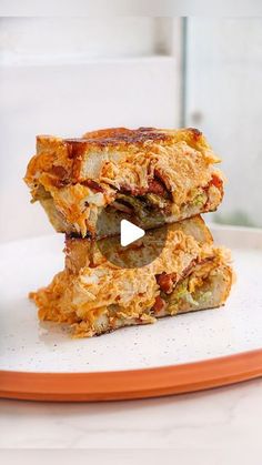 two sandwiches stacked on top of each other on an orange and white plate with a glass in the background