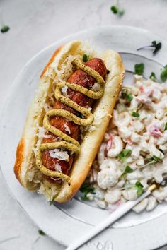 a hot dog and macaroni salad on a white plate with a silver fork