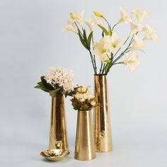 three gold vases with white flowers in them