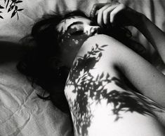 a woman laying on top of a bed next to a tree shadow painted on her body