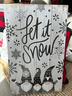 a wooden sign that says let it snow with two gnomes and snowflakes