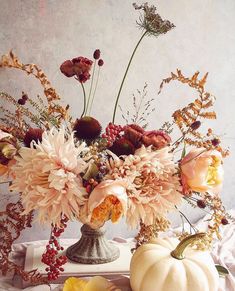 a vase filled with lots of flowers sitting on top of a white table covered in leaves