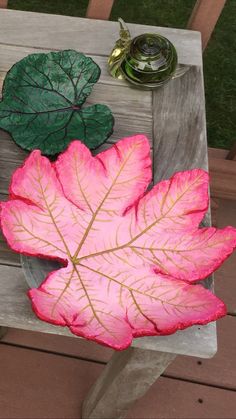 a pink and green leaf sitting on top of a wooden bench next to a cup