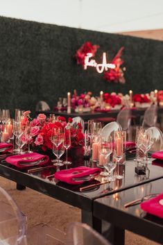 the table is set with pink and red plates, wine glasses, and candles on it