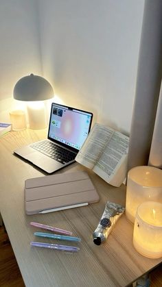 an open laptop computer sitting on top of a wooden desk next to a lit candle