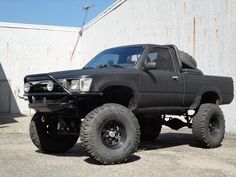 a large black truck parked in front of a building with big tires on it's tires