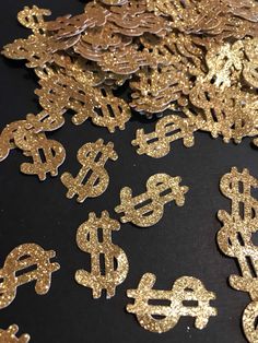 gold dollar signs are scattered on a black surface with golden sequins around them