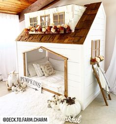 a doll house made out of wood and white with pink pillows on the floor next to it