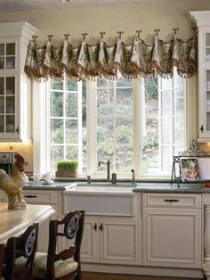 a kitchen with white cabinets and an island in front of a window that has curtains on it