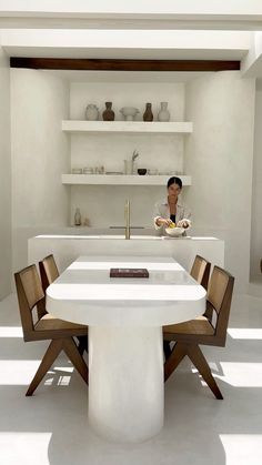 a person sitting at a table in a room with white walls and shelves on the wall