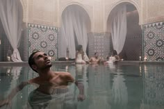 a man sitting in the middle of a swimming pool surrounded by white curtains and candles