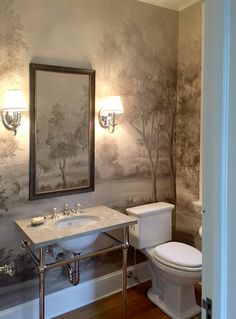 a bathroom with a toilet, sink and mirror in the corner next to a wallpapered wall