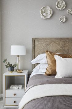 a bed with white and gold pillows on top of it next to a night stand