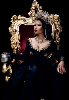 a woman in a black dress sitting on a gold throne with her hands out to the side