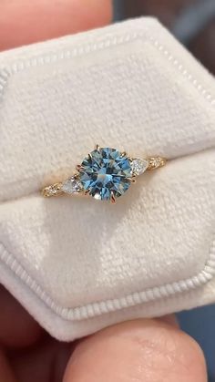 a person holding a ring with a blue stone in it's center and two diamonds on the band