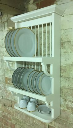 a white shelf with plates and cups on it in front of a brick wall next to a brick wall