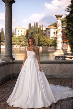 a woman in a white wedding dress standing on a stone walkway next to a lake