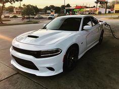 a white dodge charger parked in front of a gas station with nozzles