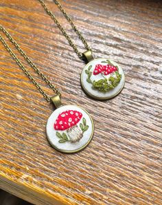 two necklaces with red mushrooms on them sitting on top of a wooden table next to each other