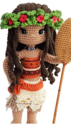 a crocheted doll holding a wooden stick and wearing a flowered headdress