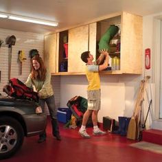 a man and woman are working on a car in a garage with tools hanging from the cabinets