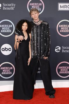 two people standing on a red carpet wearing black and white outfits, one is holding an award