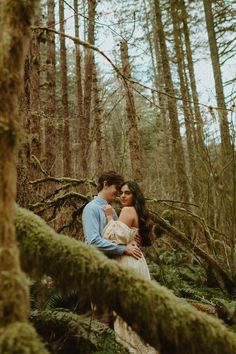 a man and woman standing in the middle of a forest with moss growing on trees