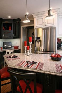 a kitchen with black cabinets and granite counter tops, red chairs around the center island