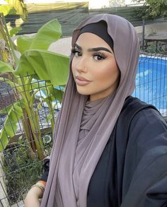 a woman wearing a hijab standing next to a pool