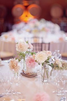 the table is set with white and pink flowers in vases, silverware and wine glasses