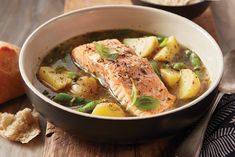 a pan filled with fish and potatoes on top of a wooden table next to bread