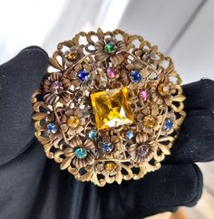 "This listing is for one Brooch : Design Number 166 : 1920's Huge  Czech Round Gilt Filigree  Brooch with a 'C' clasp fastener . There is a larger central Citrine  cushion cut stone  as well  as fifteen rhinestone centered Neiger flowers set onto the filigree  . The flowers around the main stone are onto curving filigree panels . Fleur de lis hearts around the outer edge . Set with multiple rhinestones in green , blues ,  pink , amethyst , citrine  . A very decorative Neiger Brothers quality bro